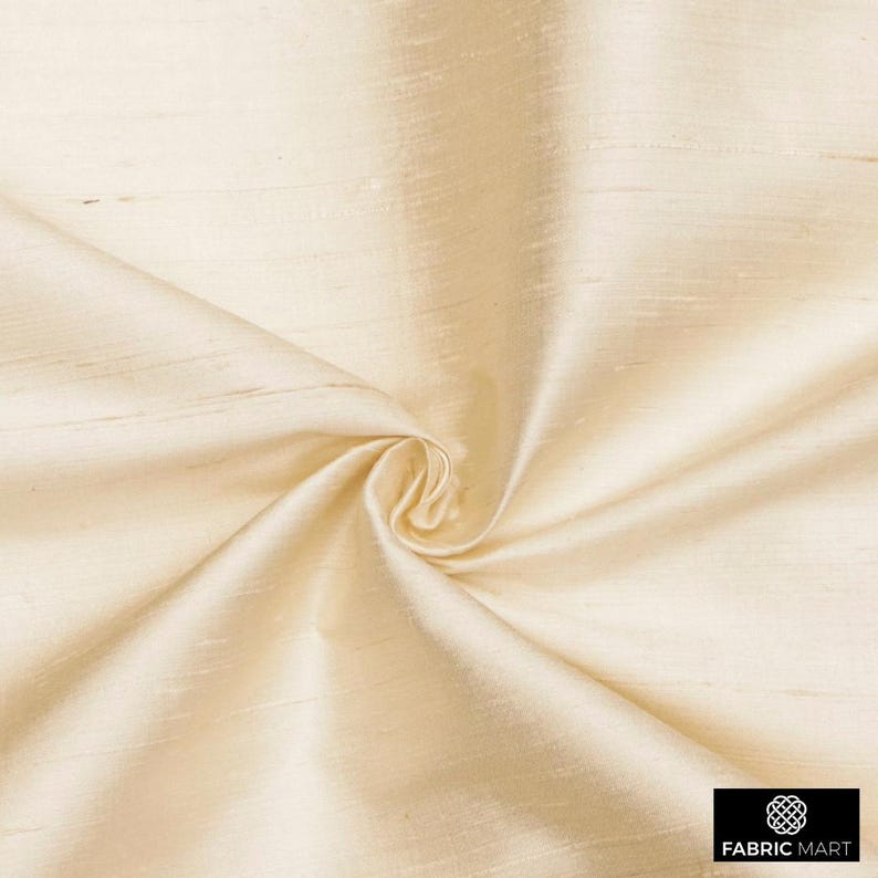 May include: Cream colored silk fabric with a subtle sheen and a smooth texture. The fabric is draped and folded, showcasing its luxurious feel.