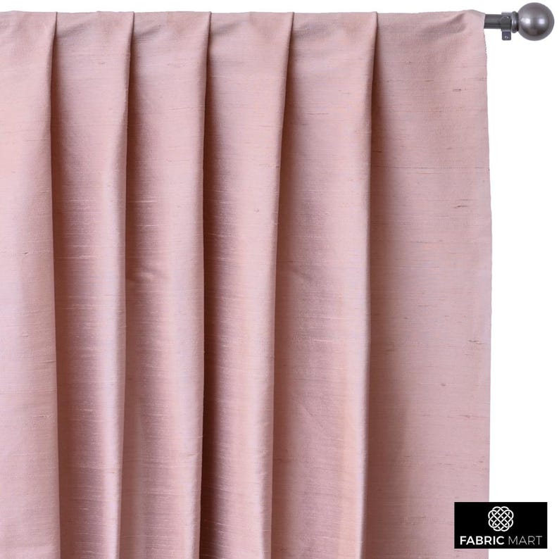 May include: A pair of blush pink curtains with pleats hanging from a curtain rod.
