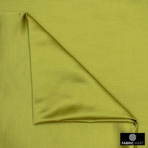 May include: A close-up of a green fabric with a subtle ribbed texture. The fabric is folded in a triangular shape, showcasing its smooth and silky finish.