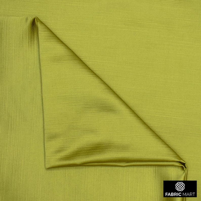 May include: A close-up of a green fabric with a subtle ribbed texture. The fabric is folded in a triangular shape, showcasing its smooth and silky finish.