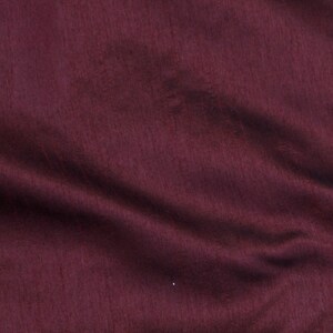 May include: A close-up of a deep burgundy fabric with a smooth, slightly textured surface. The fabric is folded and draped, creating soft folds and wrinkles.