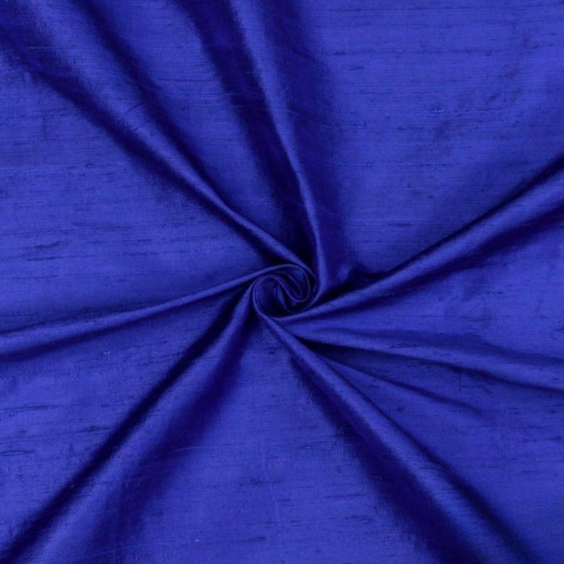 May include: A close-up of a royal blue silk fabric with a subtle sheen. The fabric is folded and draped, showcasing its soft texture and luxurious feel.
