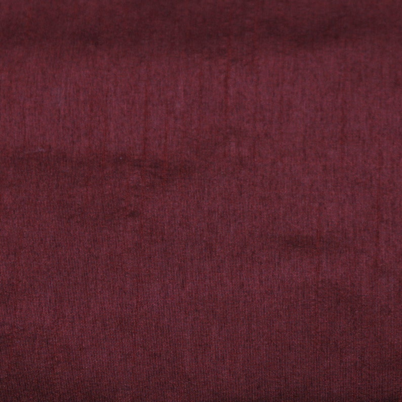 May include: A close-up of a deep burgundy fabric with a subtle texture. The fabric has a smooth, even surface with a slight sheen.