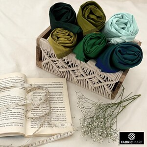 Puede incluir: Una colecci&oacute;n de seis cuadrados de tela coloridos en tonos de verde, azul y turquesa se muestran en una cesta de macram&eacute; tejida. La cesta est&aacute; hecha de fibras naturales y tiene un patr&oacute;n de diamante.
