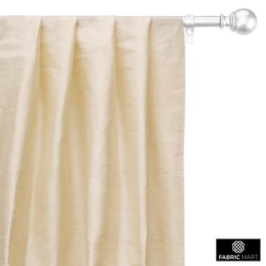 May include: A close-up of a cream-colored curtain with pleats hanging from a white curtain rod with a silver finial.