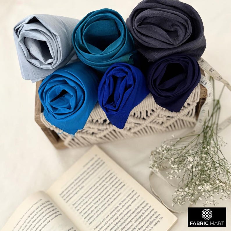 May include: Five rolls of fabric in different shades of blue, arranged in a woven basket. The fabric is soft and luxurious, perfect for crafting or sewing projects.