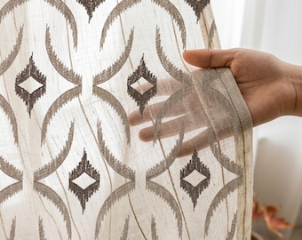 May include: A sheer, off-white curtain panel featuring a repeating dark brown geometric pattern of interlocking circles and diamond shapes. The fabric has a visible, fine-textured weave that allows light to pass through the semi-transparent material.