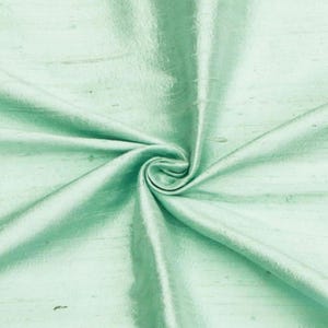 May include: A close-up of a light green fabric with a smooth, silky texture. The fabric is folded and draped, showcasing its soft and flowing nature.