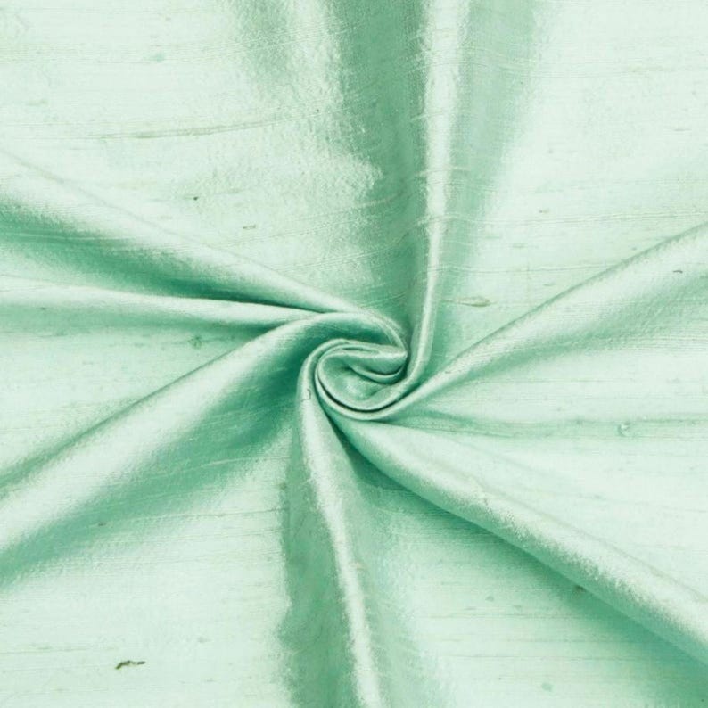 May include: A close-up of a light green fabric with a smooth, silky texture. The fabric is folded and draped, showcasing its soft and flowing nature.