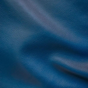 May include: A close-up of a textured blue leather fabric. The fabric has a subtle sheen and a slightly wrinkled appearance.