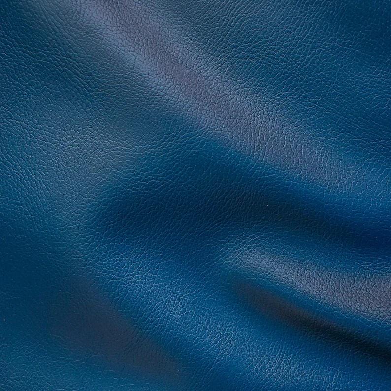 May include: A close-up of a textured blue leather fabric. The fabric has a subtle sheen and a slightly wrinkled appearance.