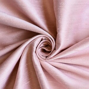 May include: Close-up of a soft, pink fabric with a subtle sheen. The fabric is draped and folded, creating a smooth, flowing texture.