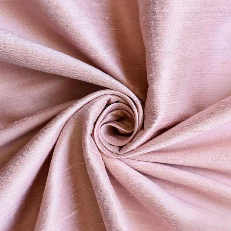 May include: Close-up of a soft, pink fabric with a subtle sheen. The fabric is draped and folded, creating a smooth, flowing texture.