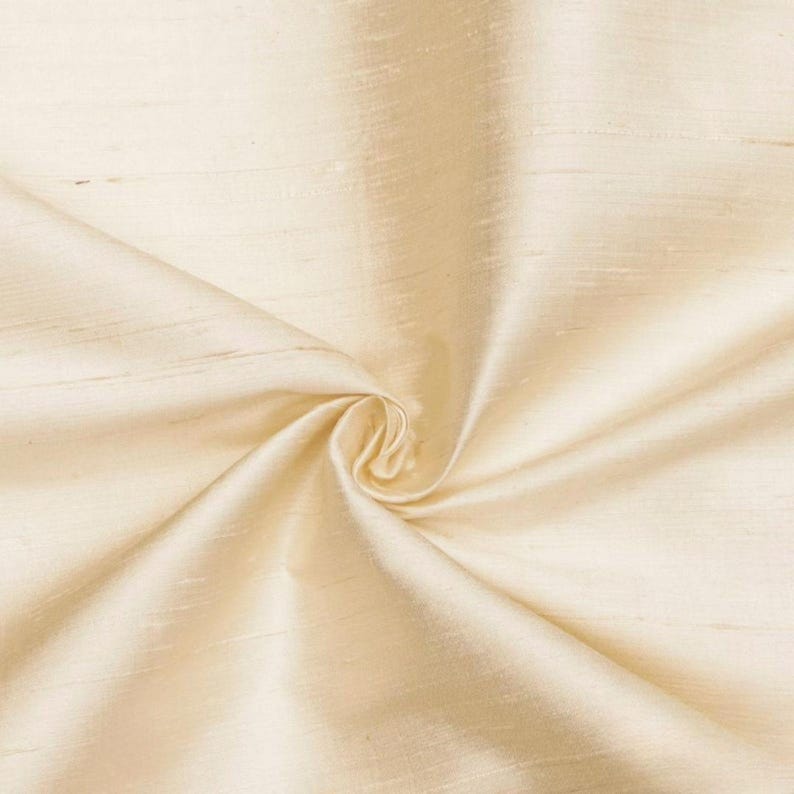 May include: Cream colored fabric with a smooth, silky texture. The fabric is folded and draped, showing its soft, flowing nature.