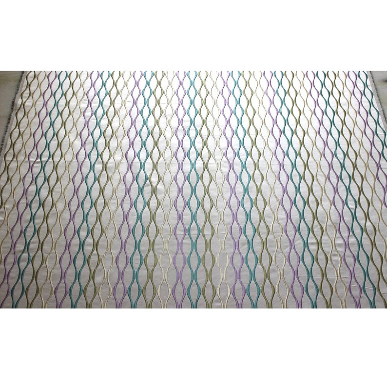 Puede incluir: Una tela blanca con un patr&oacute;n repetitivo de l&iacute;neas onduladas en tonos de verde, morado y beige.
