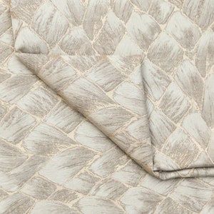 May include: Close-up of a light blue fabric with a woven pattern of beige and light brown brushstrokes. The fabric is folded in half, showing the pattern on both sides.