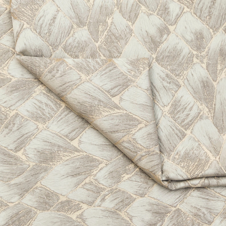 May include: Close-up of a light blue fabric with a woven pattern of beige and light brown brushstrokes. The fabric is folded in half, showing the pattern on both sides.