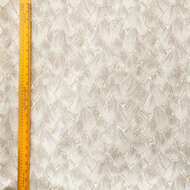 May include: A close-up of a white fabric with a textured pattern of overlapping, slightly raised, light gray leaf shapes.