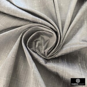 May include: Close-up of a silver silk fabric with a subtle sheen and a woven texture. The fabric is draped and folded, creating a soft, flowing look.