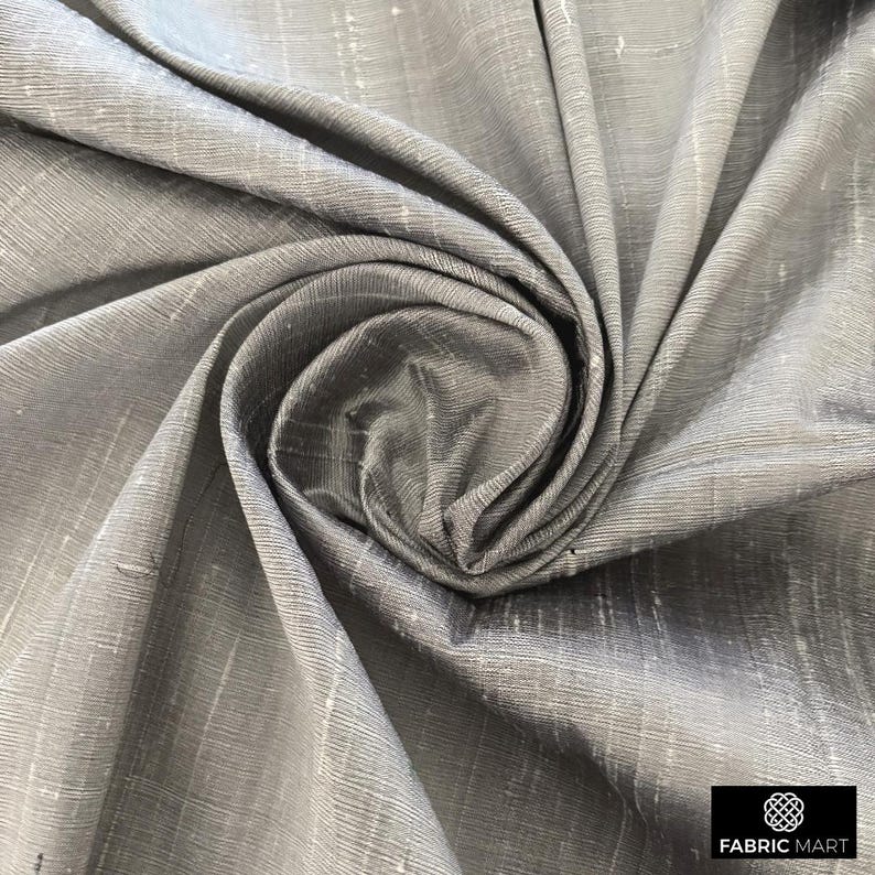 May include: Close-up of a silver silk fabric with a subtle sheen and a woven texture. The fabric is draped and folded, creating a soft, flowing look.