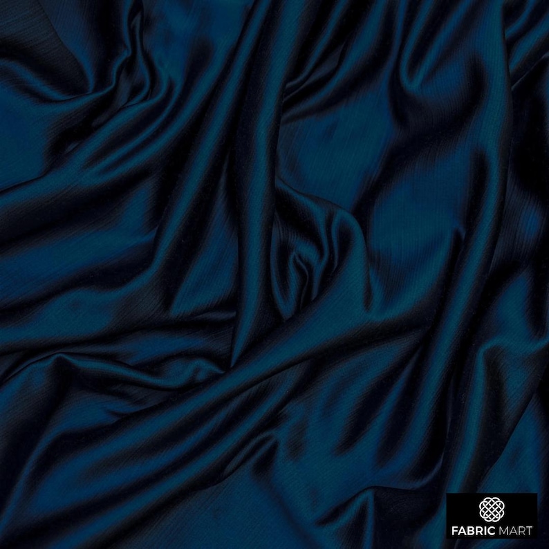 May include: Close-up of a deep blue satin fabric with a smooth, silky texture. The fabric is draped and folded, creating soft, flowing lines.
