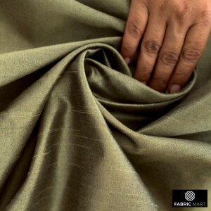 May include: A close-up of a smooth, green fabric with a subtle sheen. The fabric is draped and folded, creating a soft, luxurious look.