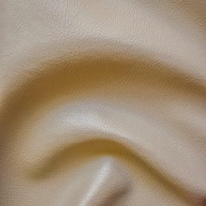 May include: A close-up of a light beige textured fabric with a subtle wave pattern. The fabric has a smooth, soft feel and a slightly shiny finish.