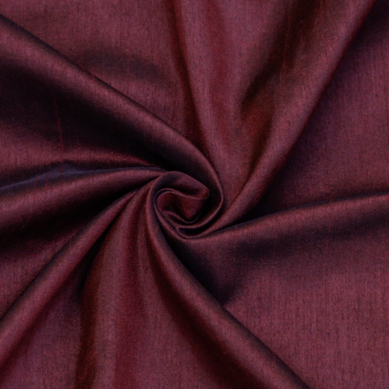 May include: Close-up of a deep burgundy fabric with a subtle sheen. The fabric is folded and draped, showcasing its soft texture.