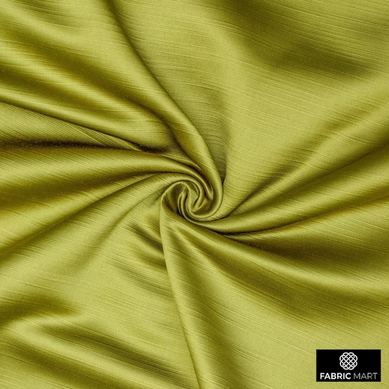 May include: Close-up of a smooth, green fabric with a subtle sheen. The fabric is draped and folded, creating a soft, flowing texture.