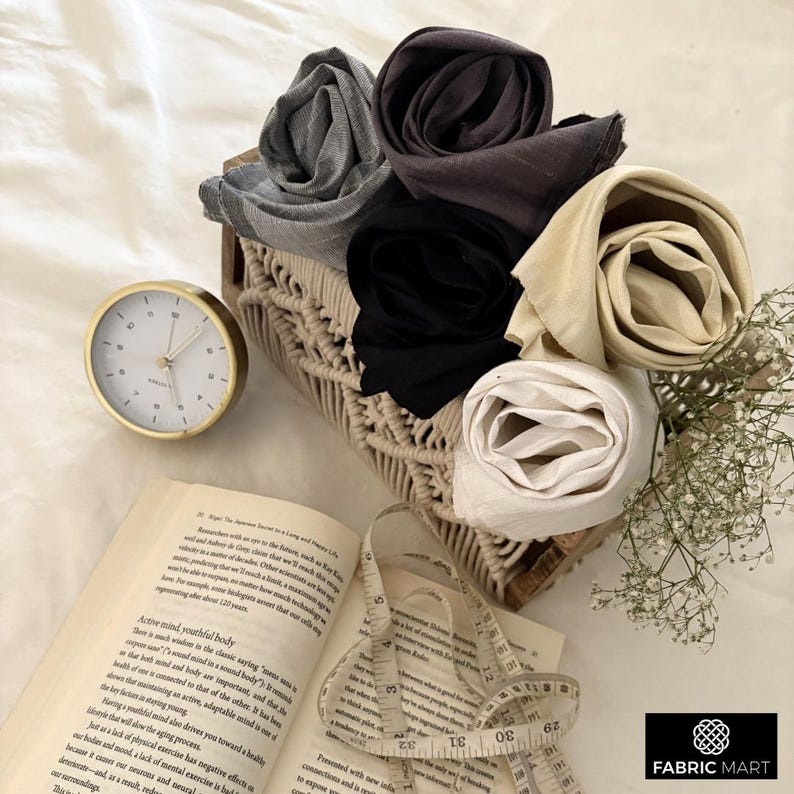May include: A set of four fabric swatches in a woven basket. The swatches are rolled up and are in the colors black, gray, beige, and white. A measuring tape and a book are in the background.