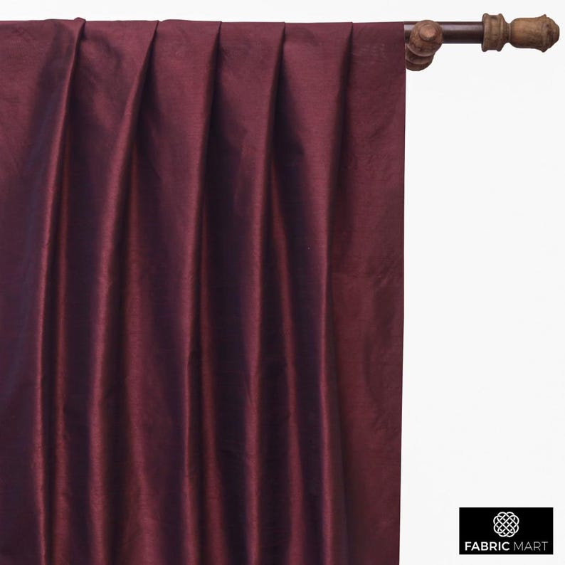 May include: Burgundy colored fabric with a silky sheen. The fabric is pleated and hangs from a wooden curtain rod.