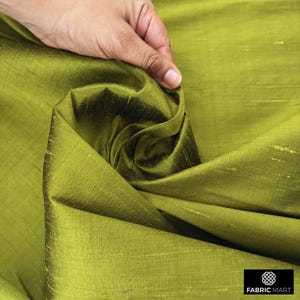 Puede incluir: Primer plano de una tela de seda verde con un brillo sutil. La tela est&aacute; doblada y drapeada, mostrando su textura y ca&iacute;da.