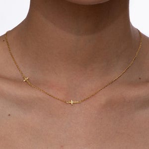 Op de afbeelding: Fijne gouden ketting met drie kleine kruisbedels. De ketting heeft een eenvoudig, elegant ontwerp, perfect voor dagelijks gebruik. De ketting is dun en de kruizen zijn gelijkmatig verdeeld.