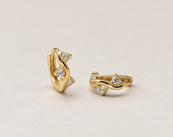 May include: A pair of gold hoop earrings featuring a wavy, open-work design. Each earring is accented with three small, clear, round-cut stones set along the curved metal frame, creating a delicate and polished appearance.