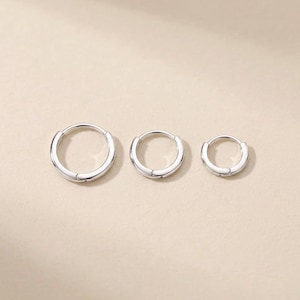 May include: Three silver hoop earrings of varying sizes are displayed against a neutral background. The earrings have a simple, polished design, with a smooth, rounded shape. The smallest earring is approximately 0.5 inches in diameter, the medium is 0.75 inches, and the largest is 1 inch.