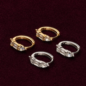 May include: Two pairs of small hoop earrings, one pair in gold-tone metal and one pair in silver-tone metal. Each hoop features a decorative setting with a clear baguette-cut stone and a clear pear-cut stone arranged side-by-side on the front.