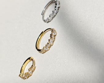 May include: Three hoop earrings arranged diagonally. The top earring is silver-toned metal with clear stones. The middle and bottom earrings are gold-toned metal, each featuring a row of marquise and round-cut clear stones along the outer edge.
