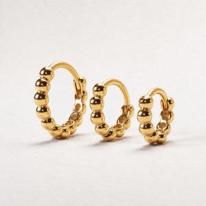 May include: Three gold hoop earrings arranged in a row from largest to smallest. Each hoop features a continuous circular design composed of small, polished, spherical gold beads connected together to form a complete ring structure.