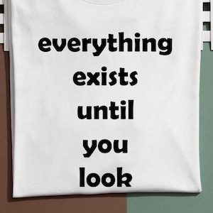 May include: White t-shirt with the text "everything exists until you look" in black, centered on the front. The shirt is displayed on a white and green surface.