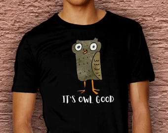 May include: Black t-shirt featuring a cartoon owl with large eyes and orange feet. The owl is brown and tan with a textured appearance. The text "IT'S OWL GOOD" is printed in white below the owl.