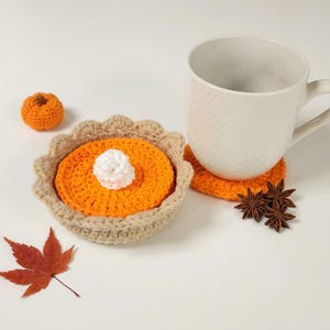 Peut inclure: Un ensemble de dessous de verre au crochet en forme de tarte à la citrouille avec une croûte beige, une garniture orange et une crème fouettée blanche. Inclut une petite citrouille au crochet, un mug blanc texturé et une feuille d'érable.