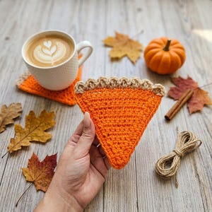 Peut inclure: Un dessous de verre en crochet triangulaire en forme de part de tarte à la citrouille avec une garniture orange vif et une croûte beige. Le dessous de verre est texturé avec des mailles et présente une bordure festonnée sur le dessus.