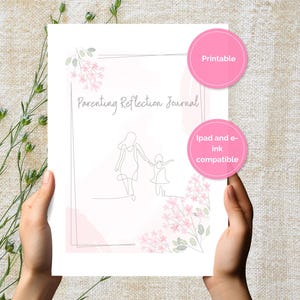 May include: A white printable journal titled "Parenting Reflection Journal" with a line drawing of a parent and child. Pink floral accents and two pink circles with text are on the page. The journal is held by hands.
