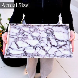May include: Rectangular serving tray with a white and purple marble design. The tray has a raised edge and the text "Actual Size!" in the upper left corner. The tray is being held by a person.