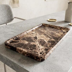 May include: A rectangular serving tray with a marble design. The tray has a brown and beige pattern with a glossy finish. The tray is on a gray surface.