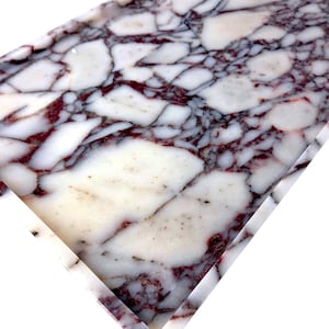 May include: Close-up of a rectangular slab of marble with a striking pattern. The marble features a white base with irregular, large patches and veins of deep burgundy and black, creating a natural, artistic design.