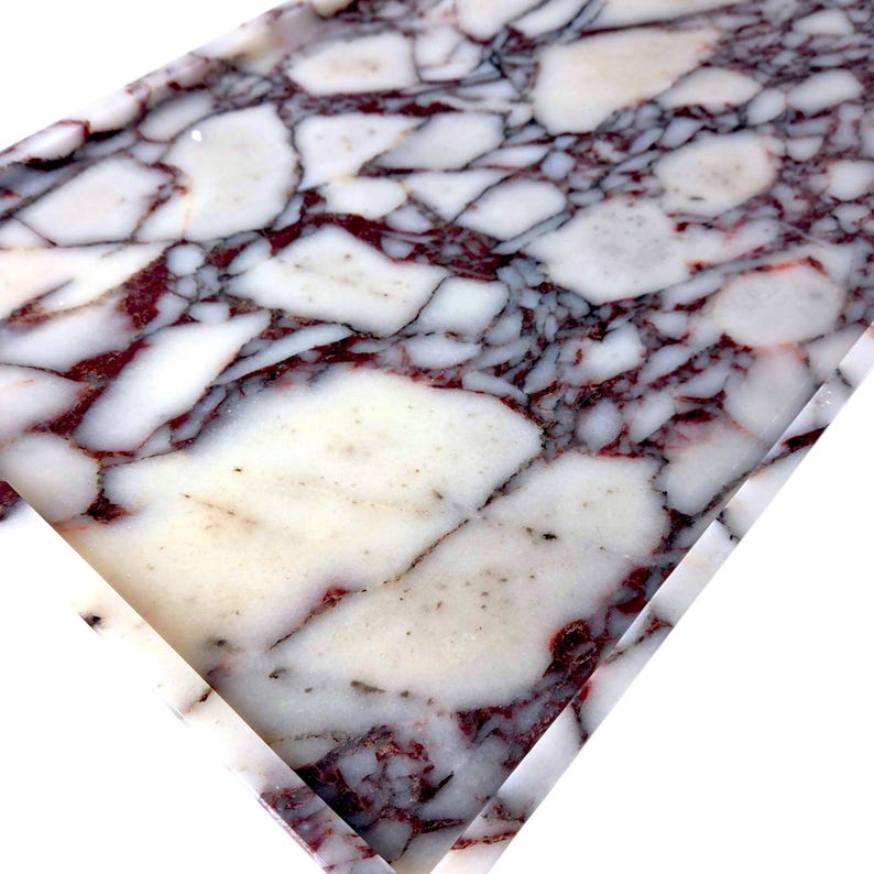 May include: Close-up of a rectangular slab of marble with a striking pattern. The marble features a white base with irregular, large patches and veins of deep burgundy and black, creating a natural, artistic design.