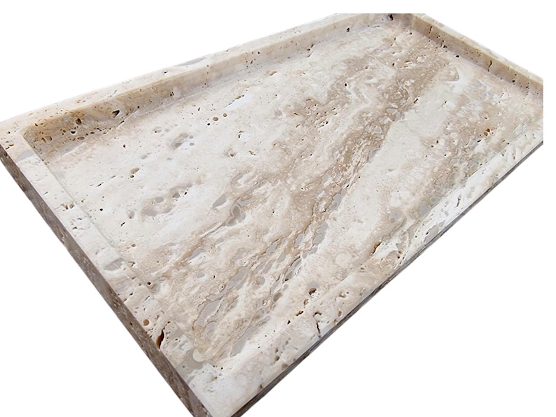 May include: Rectangular travertine tray with a raised border. The tray features a natural beige and cream color palette with unique veining patterns. Ideal for serving or decorative use.