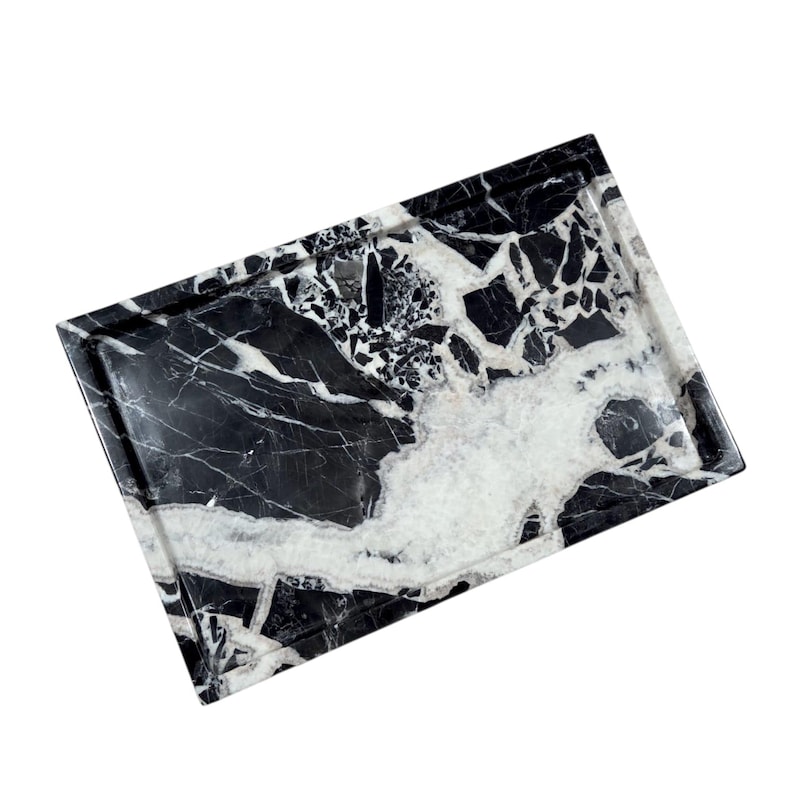 May include: Rectangular black and white marble tray with a raised edge. The tray features a striking pattern of black and white veining, creating a natural and elegant look. Ideal for serving or display.