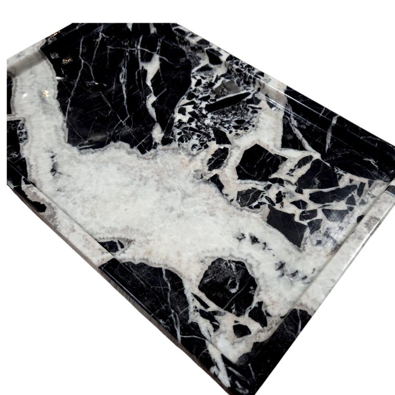 May include: A rectangular marble tray with a polished finish. The tray features a striking pattern of black and white veining, creating a natural, elegant aesthetic. The tray's edges are slightly raised, providing a defined border.